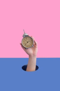 image of a hand holding an old clock in front of a dark blue and pink background. Representing the help you can get from time management coaching from a Life Coach. Who can help you identify strategies to help with time management in Salem, Oregon. 