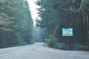 Image of a Welcome to Oregon sign in front of tall trees. Showing the you can get autism spectrum testing or ADHD testing in Oregon. No matter where you are at.